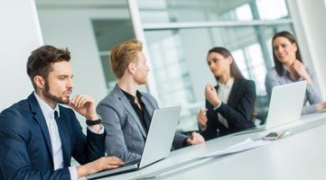 4 Personen sitzen am Tisch, teilweise mit Laptop